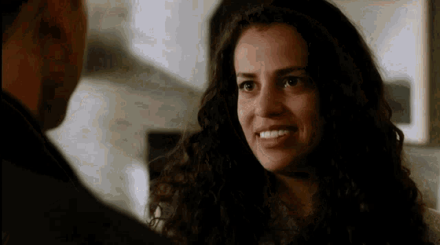 a woman with curly hair is smiling at a man in a dark room .