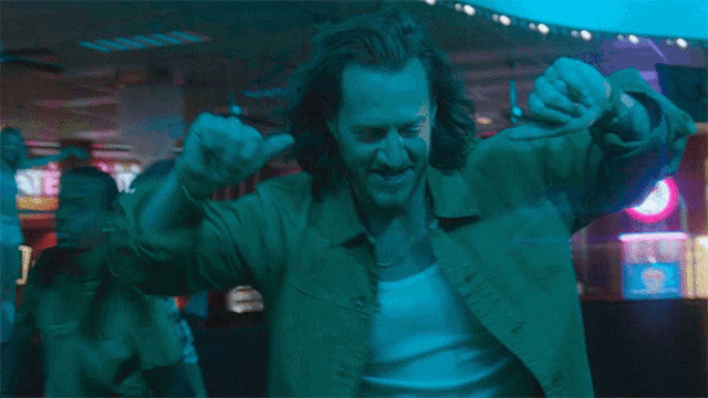 a man wearing a green jacket is dancing in a dark room