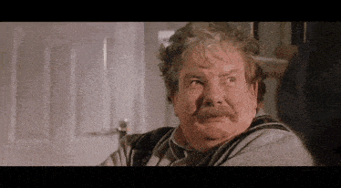 an older man with a mustache is sitting in front of a door .