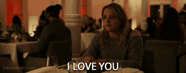 a woman is sitting at a table with a glass of wine and says i love you