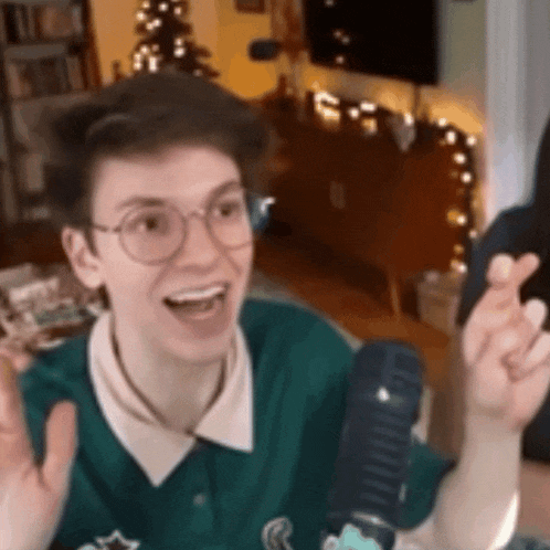 a young man wearing glasses and a green shirt is sitting in front of a microphone and making a funny face .