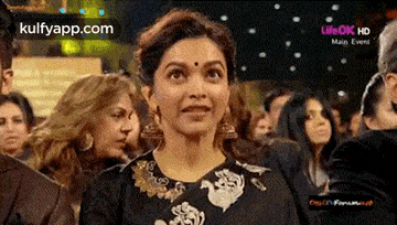 a woman with a bindi on her forehead is standing in a crowd of people .