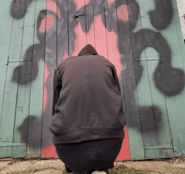 a person is kneeling in front of a wooden door that has graffiti on it