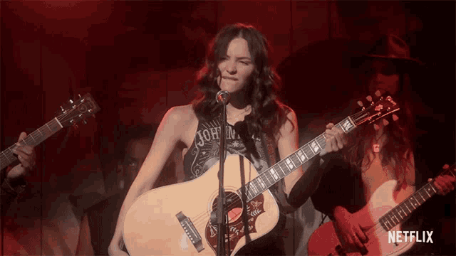 a woman singing into a microphone while holding a guitar with a netflix logo in the corner