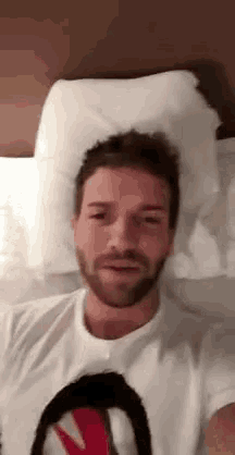 a man with a beard is laying on a bed with a white pillow on his head .