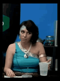 a woman in a blue top is sitting at a table with a cup of water