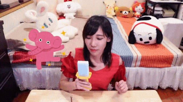 a woman is sitting at a table with stuffed animals on the bed in the background .