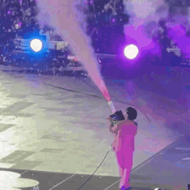 a man in a pink shirt is holding a confetti cannon on stage