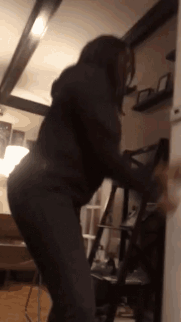 a woman in a black hoodie is standing in a room holding a ladder