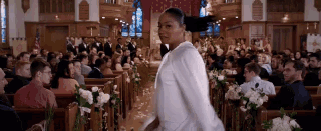 a woman in a white shirt is walking down the aisle of a church filled with people .