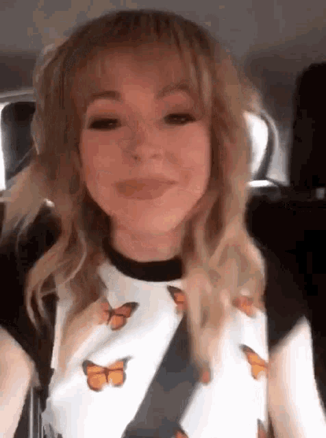 a woman in a car wearing a shirt with butterflies on it is smiling .