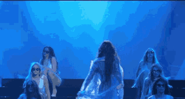a group of women are dancing on a stage in front of a blue light