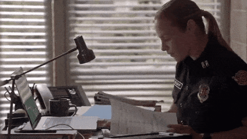 a woman in a police uniform is sitting at a desk with papers and a laptop