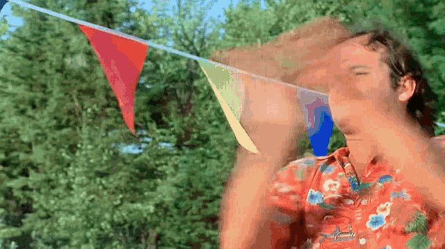 a man in a hawaiian shirt is standing in front of a string of colorful flags