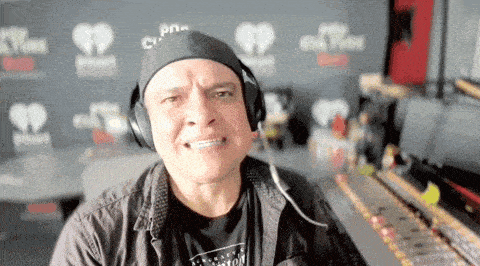 a man wearing headphones making a funny face in front of a wall that says iheart radio
