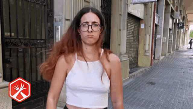 a woman wearing glasses and a white tank top is walking down the street