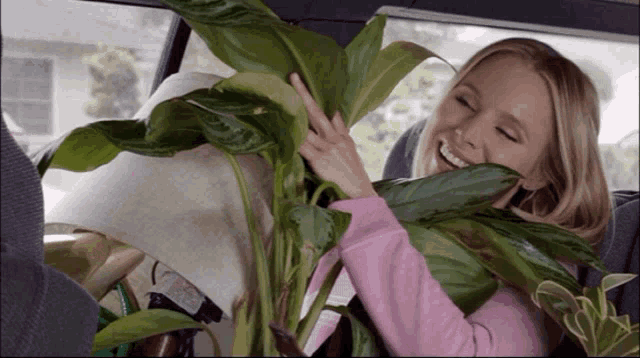 a woman in a pink shirt is holding a large plant