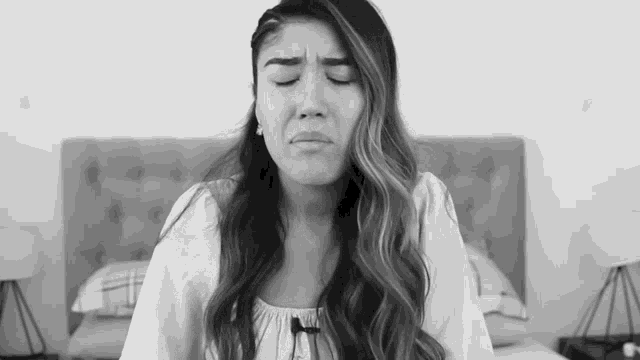 a woman is sitting in front of a bed with her eyes closed and making a funny face .