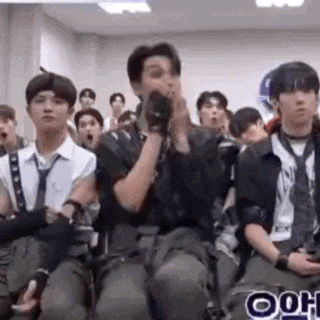 a group of young men are sitting in a room with their hands in their mouths .