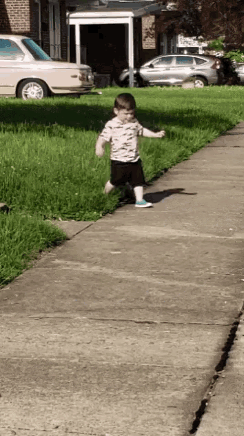 a young boy walking down a sidewalk with a car parked behind him