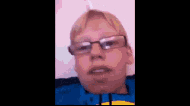 a young boy wearing glasses and a blue shirt is talking to the camera .