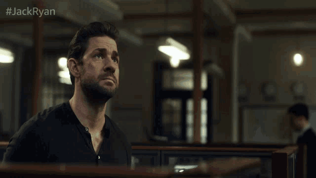 a man in a black shirt stands in a dark room with #jackryan on the bottom