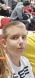a young boy is sitting in a crowd of people and making a funny face .