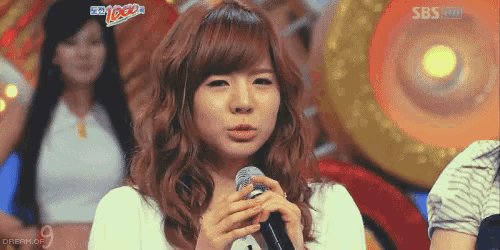 a girl singing into a microphone with sbs on the bottom right
