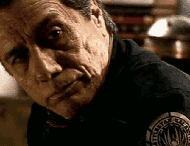a close up of a man 's face wearing a black shirt with a badge on his shoulder