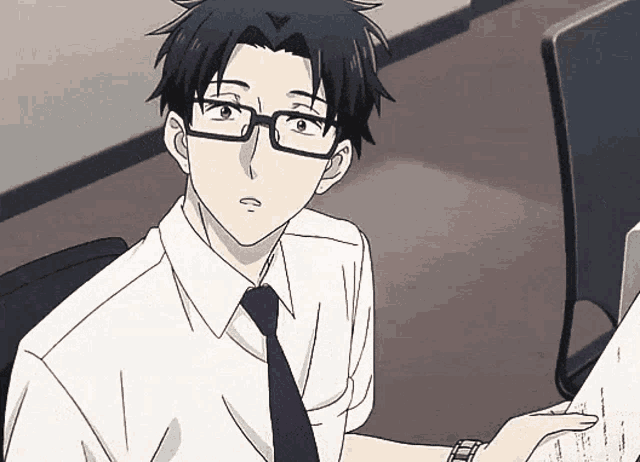 a man wearing glasses and a tie is sitting at a desk with a computer .