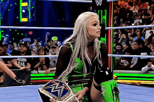 a woman is holding a wrestling championship belt in a ring .