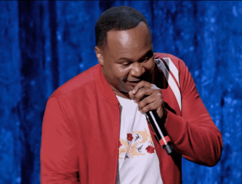 a man in a red jacket is singing into a microphone on a stage