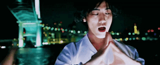 a man is standing in front of a bridge at night with his hands folded in front of his face .