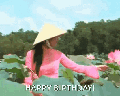 a woman wearing a pink dress and a conical hat is standing in a field of water lilies .