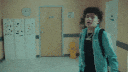 a man in a blue jacket is standing in a hallway with a clock in the background
