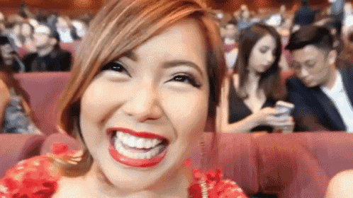 a woman in a red dress is smiling while sitting in a theatre .