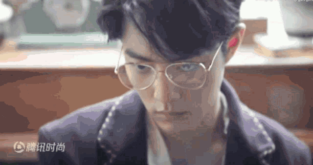 a young man wearing glasses and a purple jacket is looking at something .