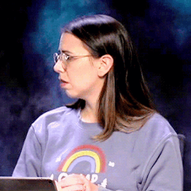 a woman wearing glasses and a sweatshirt with a rainbow on it is holding a tablet