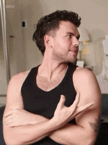 a man in a black tank top is sitting with his arms crossed .