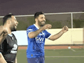 two men are playing soccer on a field and one is wearing a blue shirt that says san