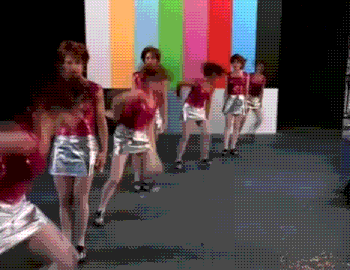 a group of women are dancing on a stage in front of a television screen .
