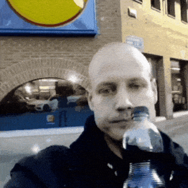 a bald man is drinking from a plastic bottle