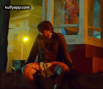 a man is sitting on a bench in front of a phone booth at night .