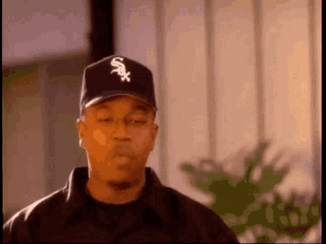 a man wearing a white sox hat is looking at the camera .