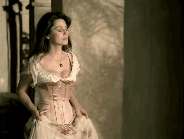 a woman wearing a corset and a necklace stands next to a wall