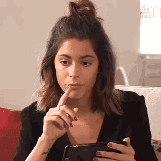 a woman is sitting on a couch looking at her cell phone and making a funny face .