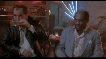 two men are sitting at a table in a bar drinking a drink .