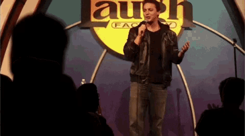 a man stands on stage in front of a sign that says laugh factory