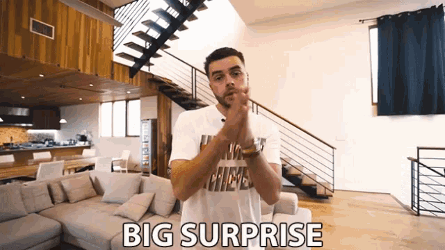 a man in a nike shirt is standing in a living room with the words big surprise written on the bottom