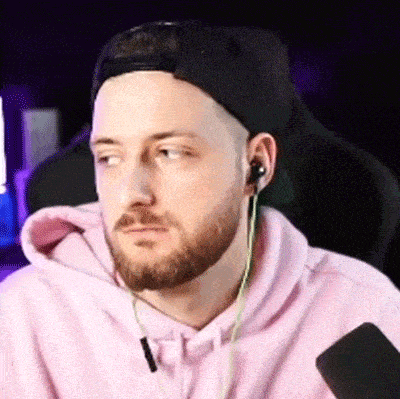 a man with a beard wearing a pink hoodie and a black hat is sitting in a chair .